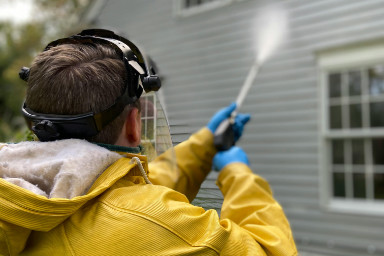 A man power washing the siding of a house.